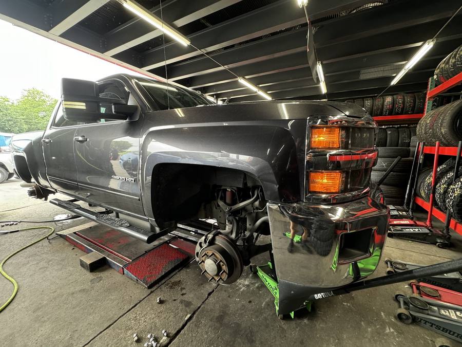 A dually pickup raised on a lift in the bay, with a deep wall of tires on racks behind it.