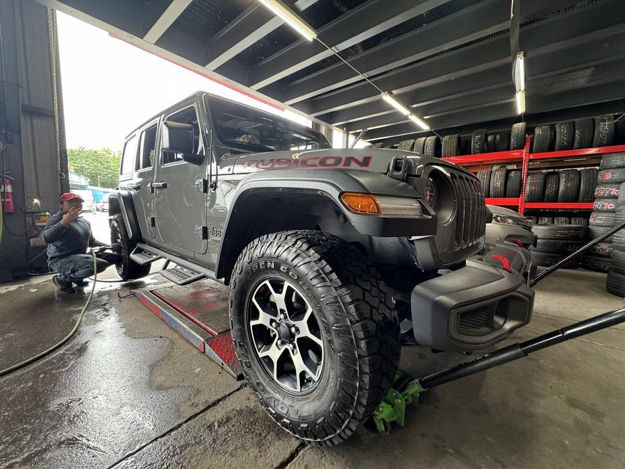 A technician in a red cap working on the wheel of a lifted Jeep Wrangler inside the service bay.