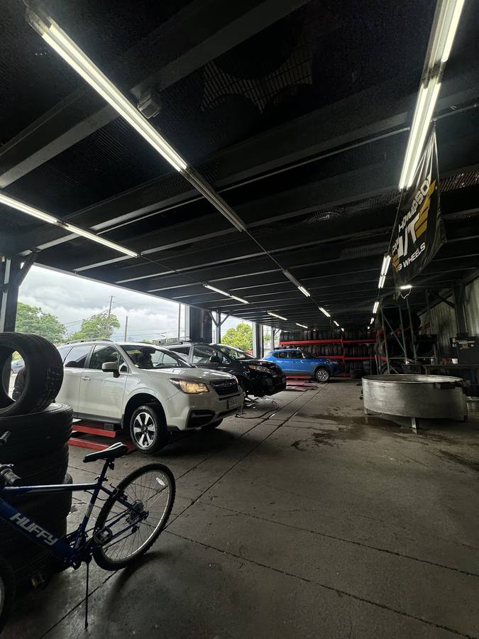 Wide view of the shop floor with three vehicles queued under the bay roof, a wall of tires on racks and stacks of used tires.